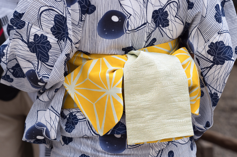 Back view of a blue-and-white floral yukata with a yellow obi featuring white geometric patterns and a light green decorative fold.